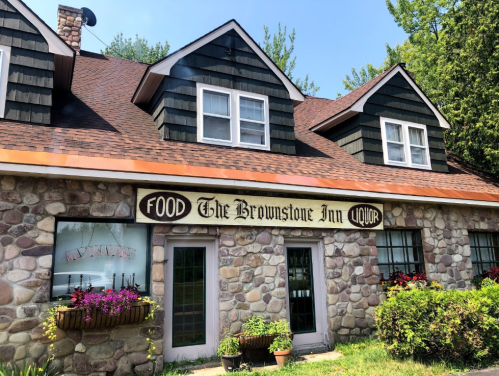 A stone building with a sloped roof, featuring signs for "The Brownstone Inn" and "Food" with flower boxes below the windows.