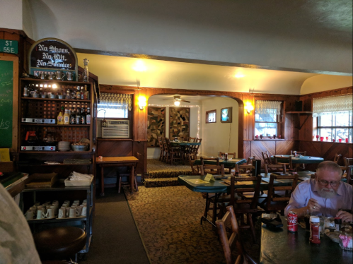 Cozy restaurant interior with wooden decor, tables set for dining, and a man sitting at a table with a drink.