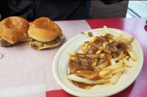 Two cheeseburger sliders and a plate of fries topped with gravy on a red table.