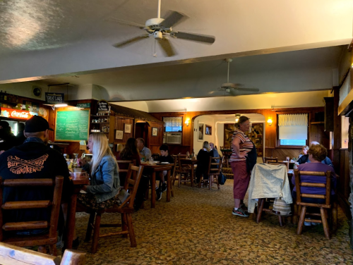 A cozy restaurant interior with wooden tables, patrons dining, and a server attending to customers.