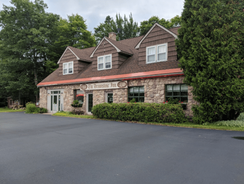 A stone and wood inn with a sloped roof, surrounded by trees and a paved parking area.