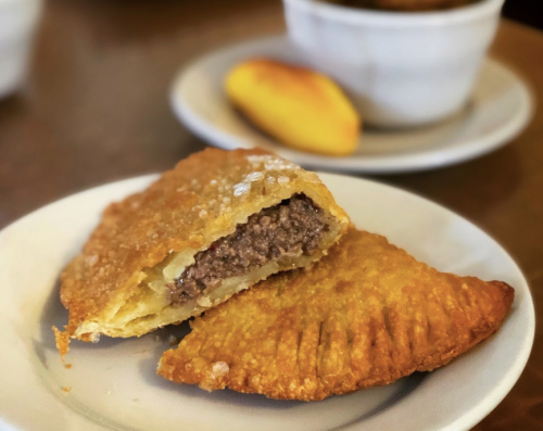 A golden-brown empanada cut in half, revealing a savory meat filling, served on a white plate.