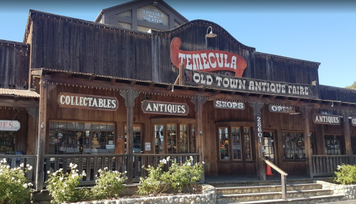 Exterior of the Temecula Old Town Antique Faire building, featuring wooden architecture and signs for antiques and collectibles.