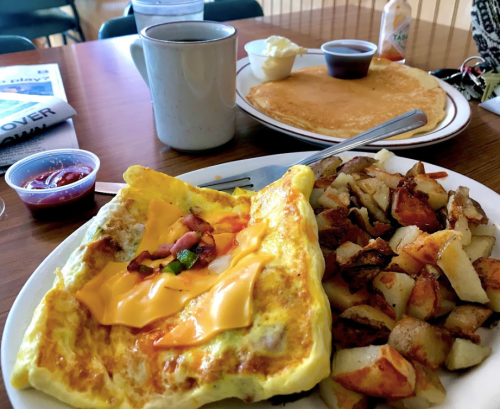 A plate of cheesy omelette, crispy potatoes, pancakes, and a cup of coffee on a wooden table.