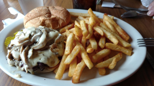 A plate featuring a cheeseburger with mushrooms, pickles, and a side of golden French fries.