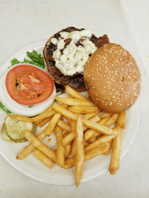 A plate with a burger topped with blue cheese, bacon, lettuce, tomato, pickles, and a side of fries.