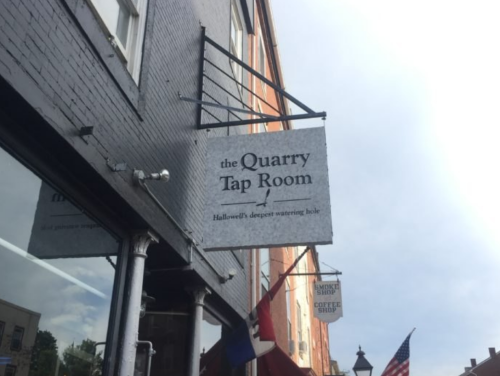 Sign for "the Quarry Tap Room," labeled as Hallowell's deepest watering hole, outside a brick building.