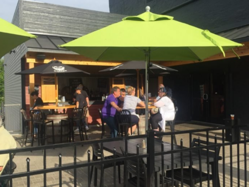 Outdoor dining area with green umbrellas, people seated at tables, and a casual atmosphere.