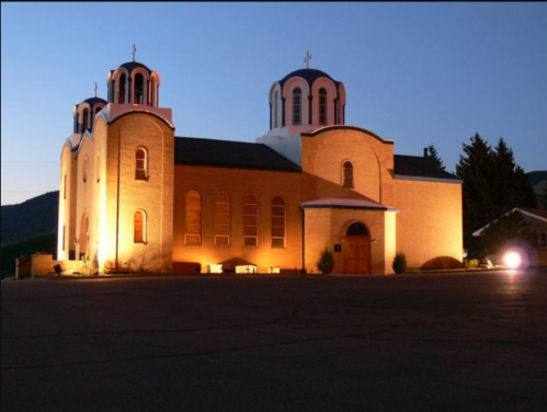 A lit-up church with two domes at dusk, surrounded by trees and a clear sky.