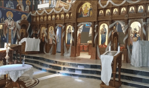 Interior of a church featuring ornate wooden altars, religious icons, and decorative drapery.
