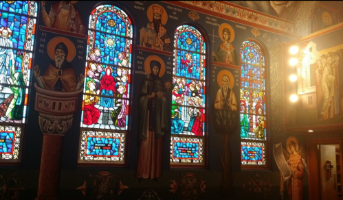 Colorful stained glass windows and religious icons adorn the walls of a beautifully decorated church interior.