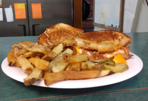 A plate with a grilled cheese sandwich and a side of crispy fries, garnished with pickles.