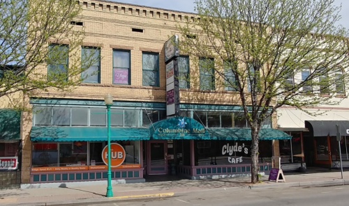 Exterior view of a brick building featuring "Columbine Mall" and "Clyde's Café," with trees lining the street.