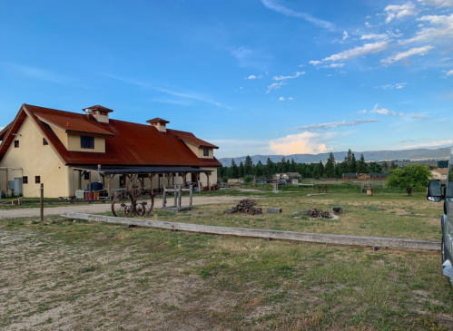 A rustic building with a red roof, surrounded by open fields and trees under a blue sky with scattered clouds.
