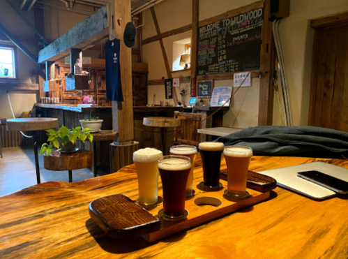 A wooden table with a flight of four craft beers in a cozy brewery setting, featuring rustic decor and a welcoming atmosphere.
