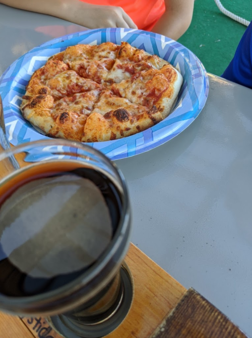 A plate of pizza slices next to a glass of dark beverage on a table.