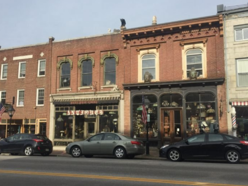 A street view of vintage shops with brick facades and parked cars along the curb.