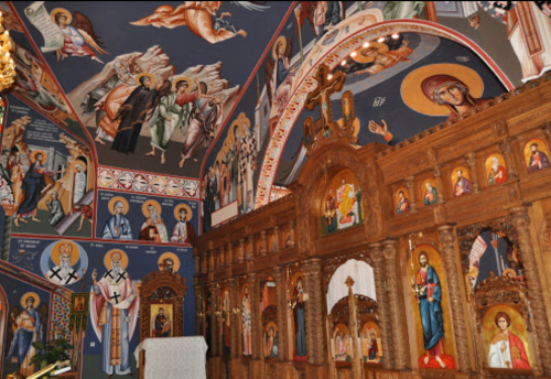 Interior of a church featuring ornate wooden icons and vibrant frescoes on the walls and ceiling.