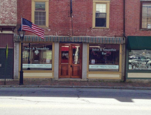 A storefront with a green awning, featuring signs for a juice and smoothie bar, and an American flag outside.