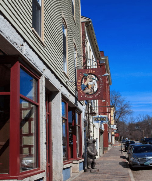 A street view featuring a café sign, a bear statue, and shops under a clear blue sky.