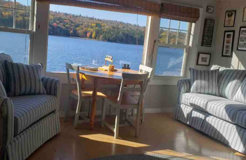 Cozy living space with striped furniture, a dining table by a lake view, and autumn foliage outside the windows.