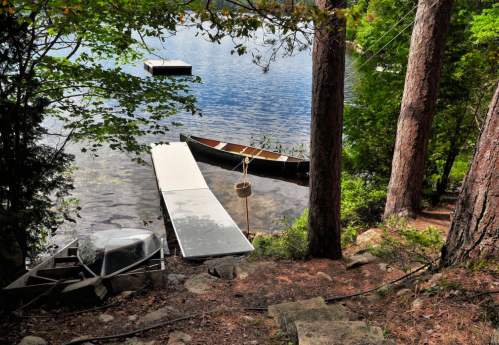 A serene lakeside scene with boats docked, surrounded by trees and calm water reflecting the sky.