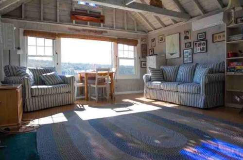 Cozy room with striped sofas, a dining table, and large windows letting in sunlight, showcasing a scenic view outside.