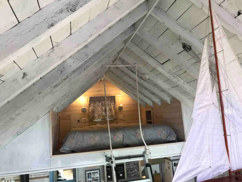 Cozy loft bedroom with a sloped ceiling, white beams, and a sailboat decoration hanging nearby.