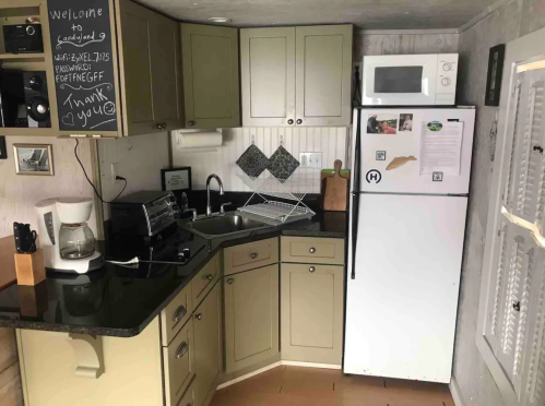 A cozy kitchen with green cabinets, a black countertop, a microwave, and a white fridge, featuring a coffee maker and decor.