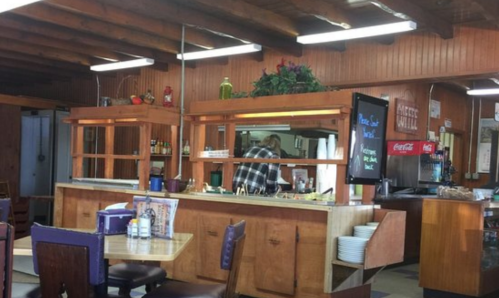 A cozy diner interior with wooden decor, a counter, and a staff member preparing food in the background.