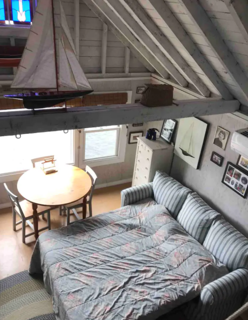 Cozy interior of a cabin with a sofa bed, dining table, and nautical decor under a sloped ceiling.