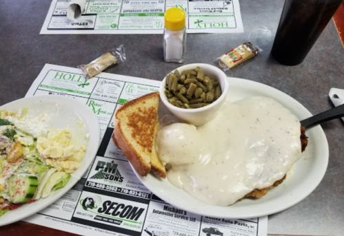 A plate of chicken with gravy, green beans, toast, and a side salad on a restaurant table with menus.