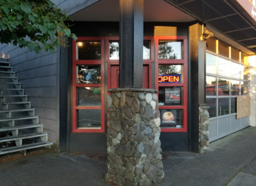 Exterior view of a restaurant with large windows, a stone pillar, and an "OPEN" sign.