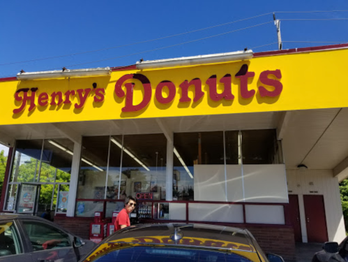 A bright yellow storefront with "Henry's Donuts" sign, featuring large windows and a clear blue sky above.