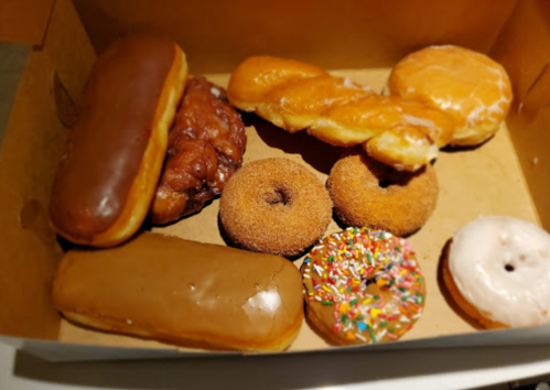A box of assorted donuts, including glazed, chocolate, and sprinkled varieties, along with a cruller and a fritter.