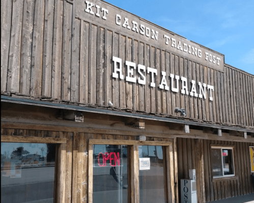 Exterior of Kit Carson Trading Post restaurant, featuring wooden siding and an "OPEN" sign in the window.