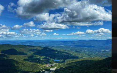 A panoramic view of lush green mountains under a blue sky filled with fluffy white clouds.