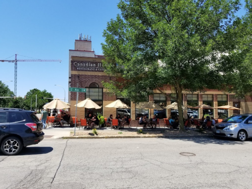Outdoor seating at a restaurant with umbrellas, people dining, and a construction crane in the background.