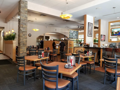 A cozy restaurant interior with wooden tables, chairs, and a stone accent wall, featuring a counter and plants.