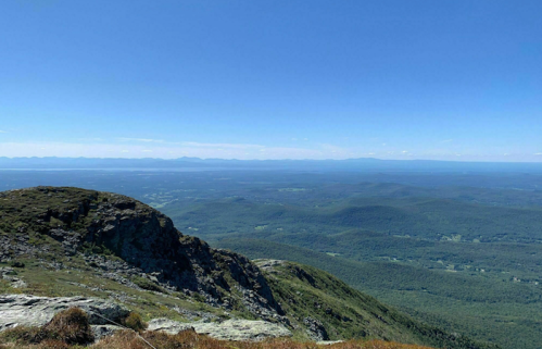 A panoramic view of rolling green hills and distant mountains under a clear blue sky.