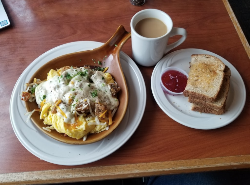 A plate of scrambled eggs topped with cheese and meat, served with toast and a cup of coffee on a wooden table.