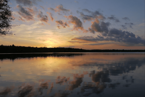 A serene sunset over a calm lake, with colorful clouds reflecting on the water's surface.