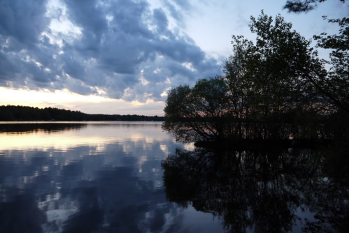 A tranquil lake at dusk, reflecting clouds and trees, with a serene atmosphere and soft colors.