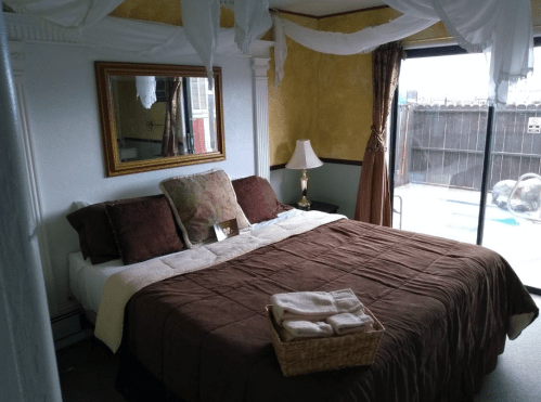 Cozy bedroom with a large bed, decorative pillows, a mirror, and a view of a pool through sliding glass doors.