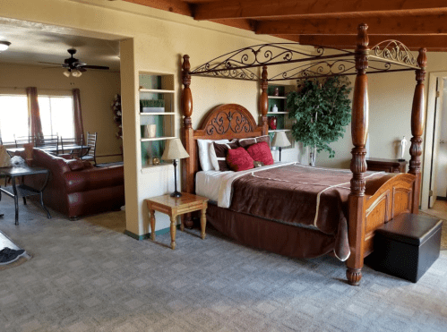 Cozy bedroom with a four-poster bed, plush bedding, and a view of a living area with a sofa and dining table.