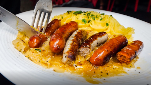 A plate of assorted sausages served with mashed potatoes and sauerkraut, garnished with herbs.