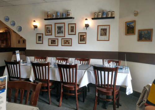 A cozy restaurant interior with wooden chairs, white tablecloths, and framed artwork on the walls.