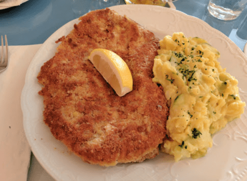 A plate featuring a golden-brown breaded cutlet with a lemon wedge and creamy scrambled eggs garnished with herbs.
