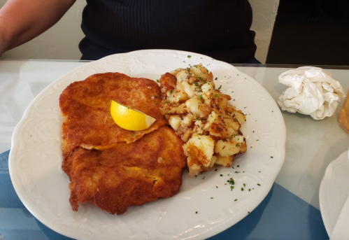 A plate with two golden-brown fried fillets, a lemon wedge, and a side of diced, seasoned potatoes.