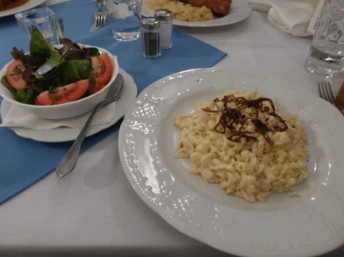 A plate of creamy pasta topped with fried onions, alongside a fresh salad with tomatoes and greens.